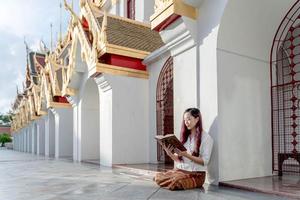 asiatische buddhistische frau, die traditionelles kleid von thailand trägt, liest sanskrit altes tripitaka-buch von lord buddha dhamma und dharma-buch, heiligtum ratchanatdaram bangkok. foto