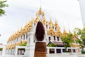 junge asiatische frau, die traditionelles kleid von thailand trägt, das am wat ratchanatdaram betet foto