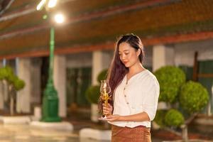 porträt asiatischer buddhistischer frau, die traditionelles kleid von thailand trägt, das kerze für beten und meditation hält foto