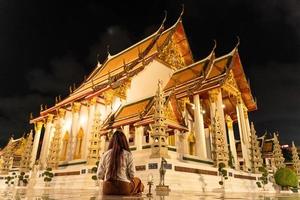 asiatische buddhistische frau, die traditionelles kleid von thailand trägt, sitzt zur meditation, um der buddha-statue im wat suthat thepwararam am buddhistischen heiligen tag, dem buddhistischen sabbattag, respekt zu zollen, foto