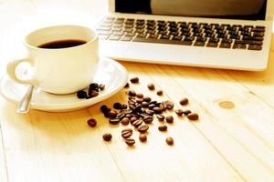 eine tasse kaffee, laptop und verteilte kaffeebohnen foto
