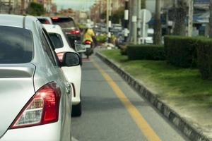 Rückseite des silbernen Autos auf der asphaltierten Straße in Richtung des Ziels der Reise. Arbeitsweg während der Hauptverkehrszeit. Umgebung verschwommen von anderen Autos in der Stadt. daneben eine Insel aus grünem Gras. foto