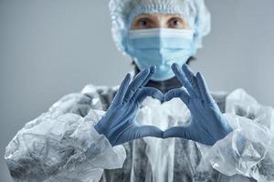 mediziner in unschärfe in medizinischer maske, gummihandschuhen und anzug macht ein herzzeichen. mit dem Coronavirus konfrontiert. foto