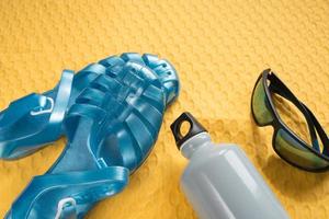 Urlaubskonzept. Sonnenbrille, Wasserflasche und Plastiksandalen für den Strand foto