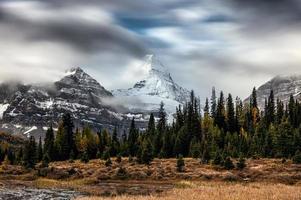 Mount Assiniboine mit Wolken, die im Herbstwald im Provinzpark durchfließen
