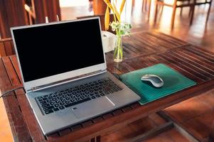 moderner Laptop mit kabelloser Maus und Blumenvase auf dem Tisch