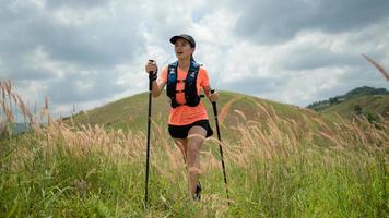 Junge Frauen, die am Nachmittag mit Trekkingstock über eine Wiese auf einem grasbewachsenen Pfad hoch in den Bergen laufen foto