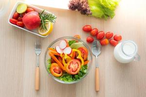 Draufsicht auf frische Gemüsesalatschüssel, gemischtes Gemüse wie Radieschen, Tomaten, Karotten, grüne Eiche, rote Eiche und Tomaten, Äpfel und Vollmilch werden darum herum zubereitet. foto