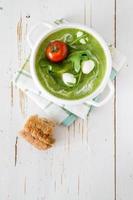 grüne reine Suppe mit Ruccola und Tomate in weißer Schüssel