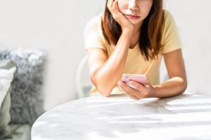 Gelangweilte junge Asiatin, die enttäuscht auf ihr Smartphone schaut, während sie auf jemanden im Restaurant wartet foto