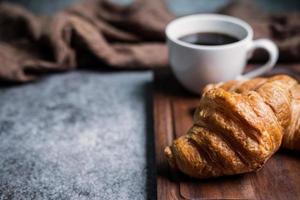 frühstück mit frischen croissants und tasse schwarzem kaffee auf holzbrett foto