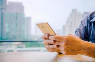 Nahaufnahme des Handys in den Händen eines Mannes, Hände eines Mannes, der ein Smartphone hält, während er in einem Café sitzt und auf ihre Bestellung wartet foto