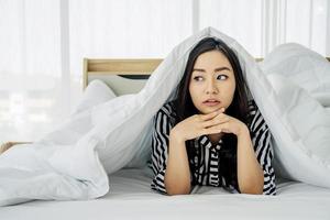 junge asiatische frau, die morgens aufwacht, lächelnde frau, die unter einer bettdecke in ihrem schlafzimmer ruht. Nahaufnahme Porträt einer schönen jungen Frau und unter der Decke. frohen guten morgen foto