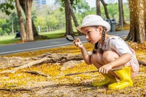 Bild eines süßen Mädchens, das die Natur mit einer Lupe im Freien erkundet, ein Kind, das im Wald mit einer Lupe spielt. Neugieriges Kind, das mit der Lupe auf dem Gras im Park sucht foto