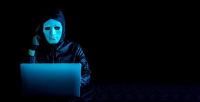 hacker in weißer maske und hoodie, der mit einem laptop im netz surft und ernsthaft über fragen, terroristen und virtuellen raum nachdenkt. Konzept der unsicheren Zone, sehr verwirrte Idee foto