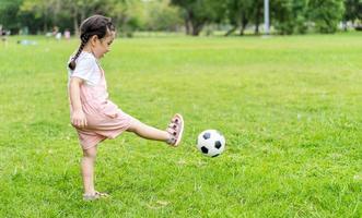 Sportkind. glückliches kleines mädchen, das einen fußball tritt, kind spielt foto