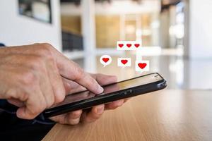 Mann Hand mit Smartphone mit Herz-Symbol im Büro, sieht er Nachricht von Liebhabern. technologiegeschäft und soziales lebensstilkonzept.