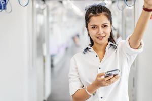 Junge asiatische Passagierin steht und benutzt Handy in leerer U-Bahn oder Sky-Train-Wagen, Freizeit und Alltag foto