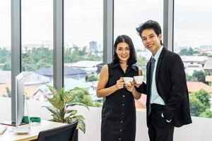 schöne kaffeepause, geschäftsfrau trinkt einen espresso während eines kleinen gesprächs mit einem jungen kollegen, während sie im büro steht foto