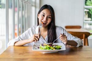 porträt einer attraktiven asiatischen lächelnden jungen frau, die salat im restaurant isst, ein junges glückliches mädchen, das ein gesundes mittagessen hat foto