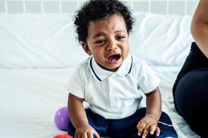Nahaufnahme eines entzückenden kleinen afroamerikanischen Jungen, der auf dem Bett weint - schwarze Menschen foto