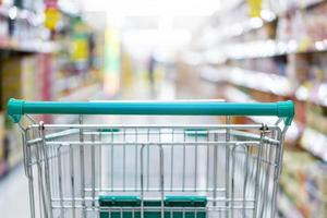 Einkaufswagen im Supermarktgang mit Produktregalen innen defokussiert, unscharfer Hintergrund foto