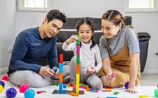 Familien- und Kindheitskonzept. junge familie verbringt zeit im spielzimmer. asiatischer vater, mutter und tochter sitzen auf dem boden und spielen mit bunten blöcken foto