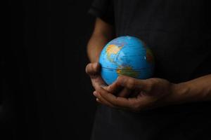 Blick aus der Vogelperspektive auf Hände, die einen Globus auf schwarzem Hintergrund halten. earth day-konzept mit zurückhaltendem tonfoto foto