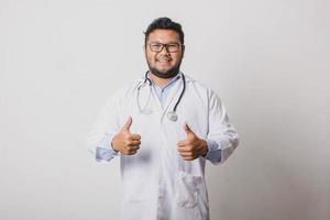 fröhlicher männlicher Arzt mit Daumen nach oben Bewegung beider Hände isoliert auf weißem Hintergrund foto