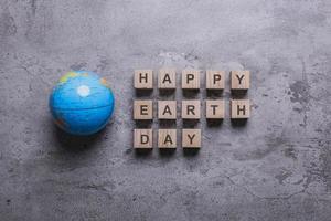 flache Laienzusammensetzung des Globus mit Happy Earth Day-Zitaten auf Holzwürfel auf Zementtexturhintergrund foto