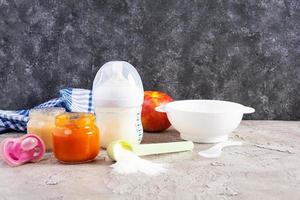 Schüssel mit Gemüsepüree und Flasche Babynahrung auf grauem Hintergrund foto