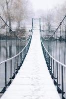 Fußgänger-Hängebrücke aus Stahl und Holz über den Fluss, Winter foto