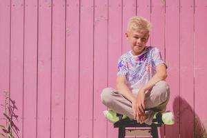 Porträt eines süßen, gutaussehenden, elfjährigen Jungen, der auf dem hölzernen lila Hintergrund im Freien sitzt. aufwachsen, sommer, freude, kindheitskonzept foto