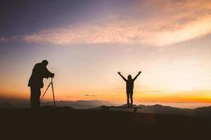 silhouette des fotografen, der bei sonnenuntergang mit dem modell auf dem berg fotografiert, professionelle hochzeitsfotografie foto