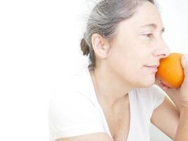 neunundvierzig Jahre alte Frau in einem weißen T-Shirt vor einem weißen Hintergrund mit einer Orange foto