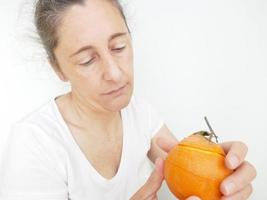 neunundvierzig Jahre alte Frau in einem weißen T-Shirt vor einem weißen Hintergrund mit einer Orange foto