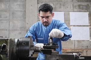 ein professioneller asiatischer männlicher industrieingenieur arbeitet in einer sicherheitsuniform mit metallbearbeitungspräzisionswerkzeugen, mechanischen drehmaschinen und einer ersatzteilwerkstatt in der stahlfabrik. foto