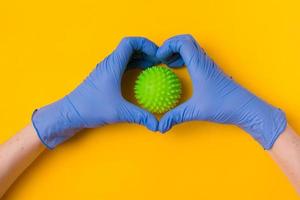 Hände in blauen OP-Handschuhen halten ein Coronavirus-Molekül auf gelbem Hintergrund. foto