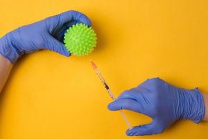 Hände in blauen OP-Handschuhen halten ein Coronavirus-Molekül auf gelbem Hintergrund. foto