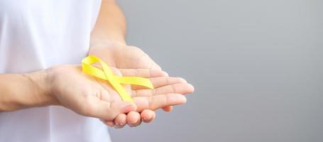 hand, die gelbes band hält, um lebende und kranke menschen zu unterstützen. september tag der selbstmordprävention, konzept des bewusstseinsmonats für kindheit, sarkom und knochenkrebs foto
