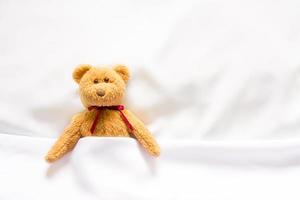 Teddybärpuppe, die im weißen Bett liegt foto