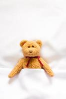 Teddybärpuppe, die im weißen Bett liegt foto