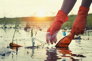 Frauenhand, die Müllplastik zur Reinigung am Fluss mit Sonnenuntergang aufsammelt foto