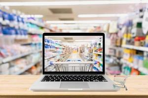 Laptop-Computer auf Holztisch mit Supermarktgang verschwommenem Hintergrund Online-Shopping-Konzept foto