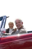 älteres Ehepaar sitzt in rotem offenem Auto, ausgeschnitten