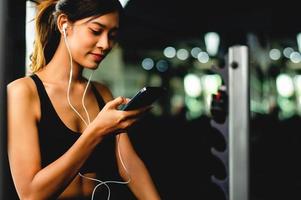 mädchen im fitnessstudio trainieren mit einem handy, das musik mit weißen kopfhörern hört und einen digitalen herzschlag-timer verwendet. systematisch ihre Urlaubsentspannung ausüben foto