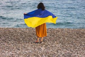 Ein Mädchen steht mit einer ukrainischen Flagge am Meer foto