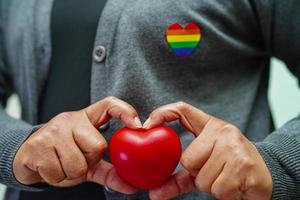 asiatische frau, die rotes hert mit regenbogenflagge, lgbt-symbolrechten und geschlechtergleichheit, lgbt-stolzmonat im juni hält. foto