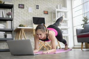 fitte junge frau, die zu hause yoga über online-unterricht mit professionellem ausbilder, sport und gesundem lebensstilkonzept praktiziert. foto