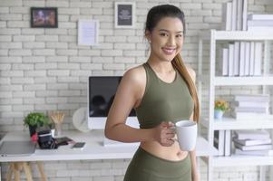 junge fitnessfrau in sportbekleidung, die nach dem training zu hause, gesund und lebensstil eine tasse kaffee trinkt. foto